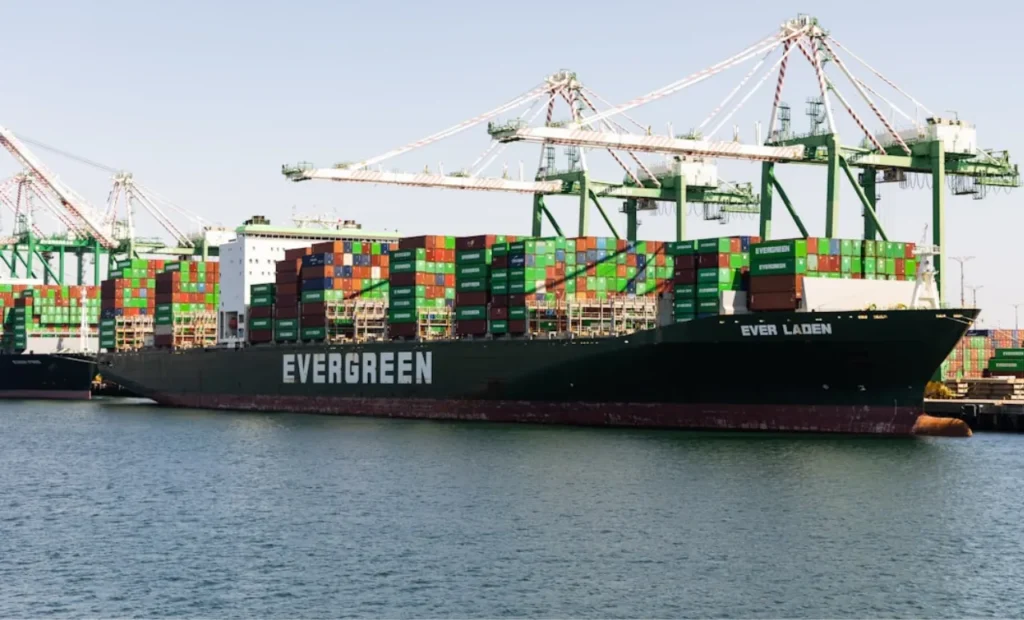 Evergreen cargo ship loaded with containers docked at a shipping port.