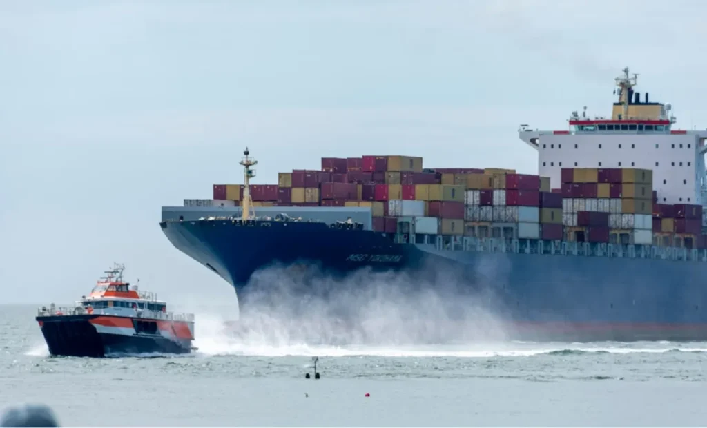 A cargo ship escorted by a small boat at the port.